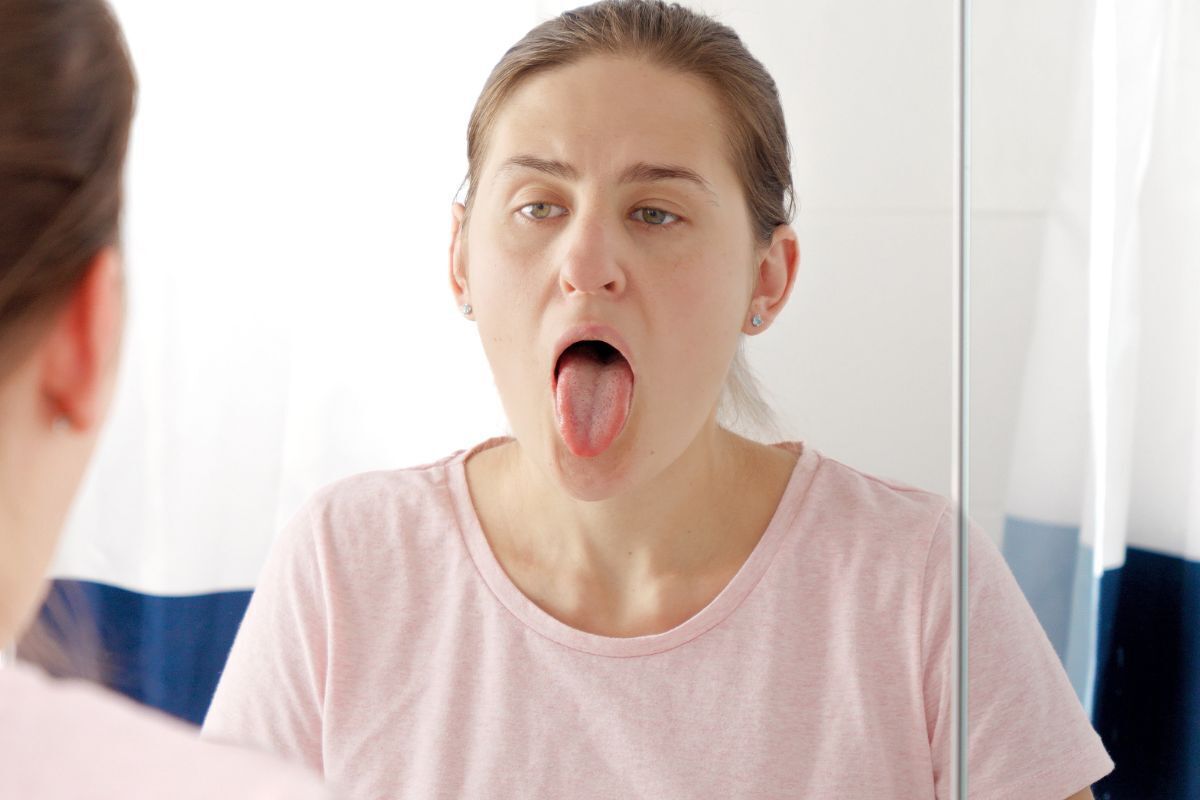 Woman examining her tongue in mirror, checking for lumps or oral abnormalities.