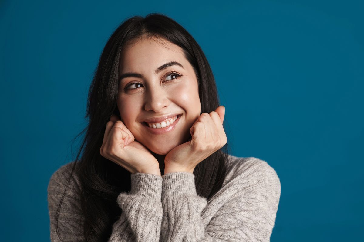 Smiling woman in gray sweater showcasing a bright, healthy smile against blue background.
